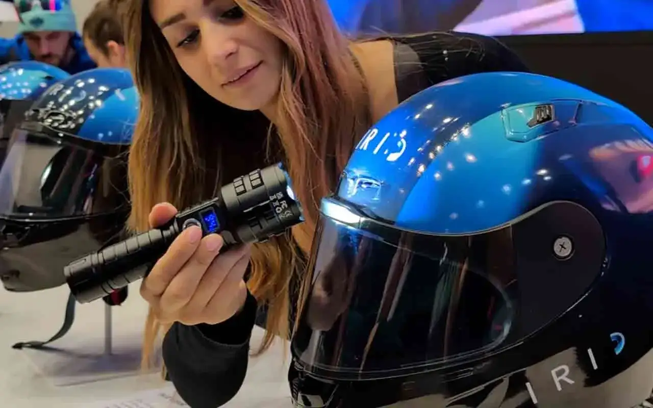 Donna esamina un casco da moto blu con visiera, tenendo in mano una torcia. È bene che il casco sia dotato di visiera per proteggere gli occhi.