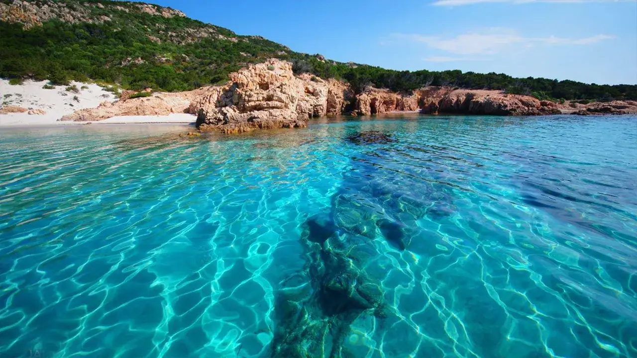 Acque cristalline e sabbia bianca a Cala Soraya, un angolo di paradiso con rocce rosse e vegetazione mediterranea.