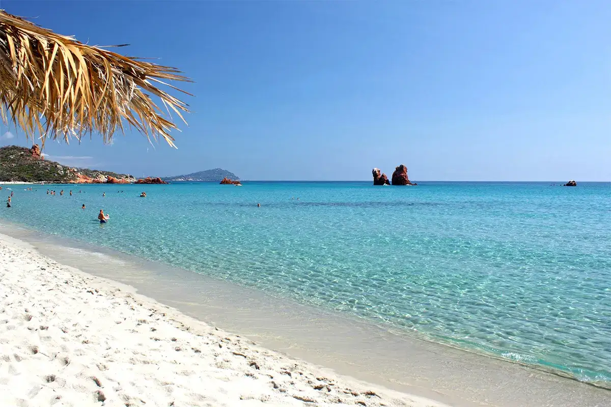 Spiaggia di Arbatax, dove si trova la Sardegna, con rocce rosse nel mare cristallino e gente che nuota.