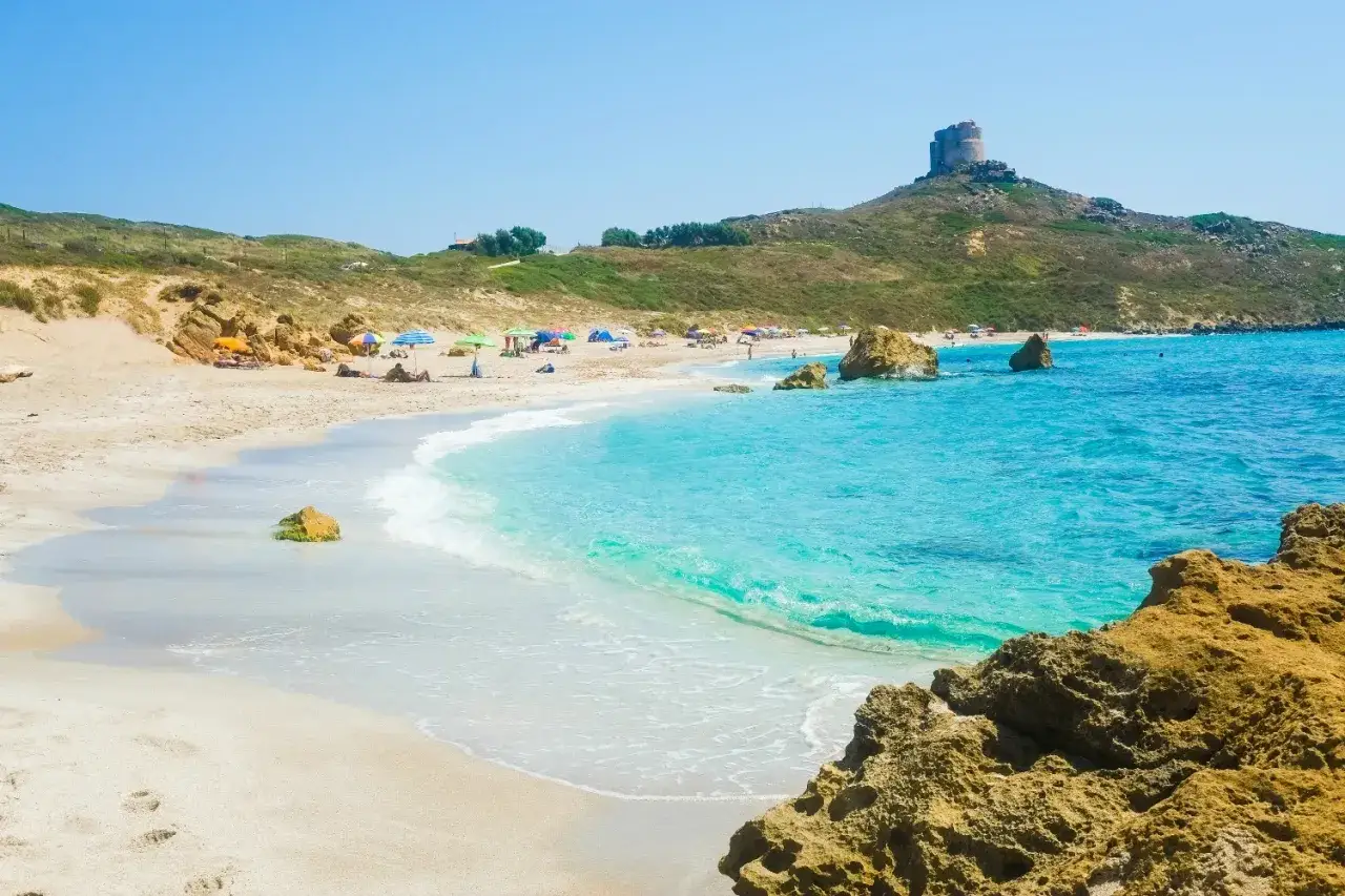 Spiaggia di Is Arutas, Cabras, con torre antica su collina. Acqua cristallina e sabbia bianca.