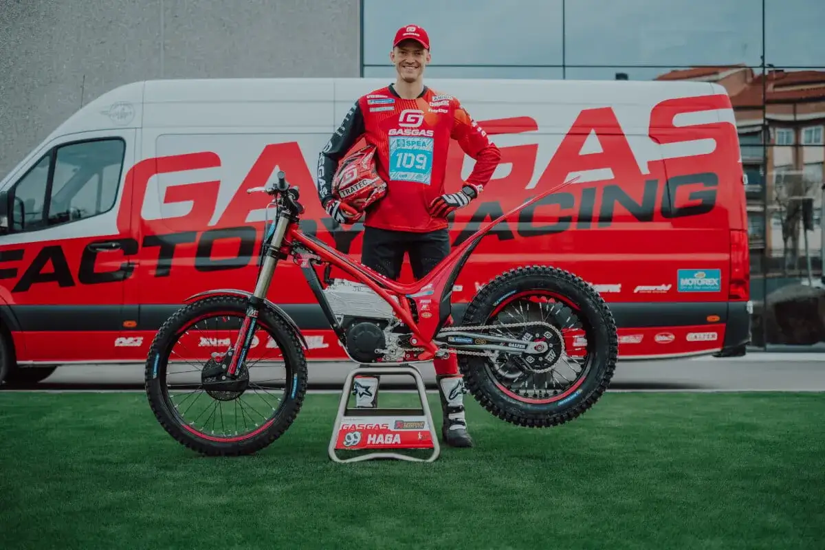 Pilota Gas Gas con moto da trial rossa, pronto a dare gas. Furgone rosso con logo Gas Gas sullo sfondo.