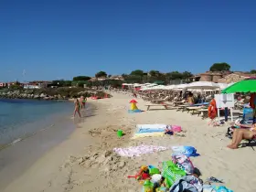 A sunny beach with people walking in the shallow water and lounging under umbrellas.