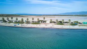 Spiaggia di Putzu Idu con palme, camper e gente che si gode il sole. Acqua cristallina e cielo azzurro.