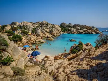 Una baia con rocce granitiche scolpite dal vento e acque turchesi cristalline, tra le spiagge più belle sardegna nord. Gente rilassata sotto gli ombrelloni.