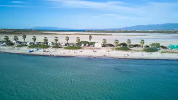 Spiaggia di Putzu Idu con palme, camper e gente che si gode il sole. Acqua cristallina e cielo azzurro.
