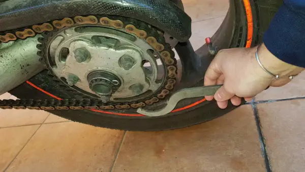 Mano con chiave inglese che lavora sulla catena di una moto, mostrando come tirare la catena della moto per la manutenzione.