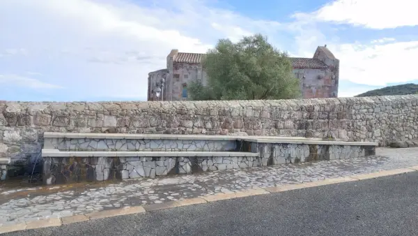 Fontana in pietra con scorci di un antico edificio religioso, un'oasi di pace ad **Allai, Sardegna**.