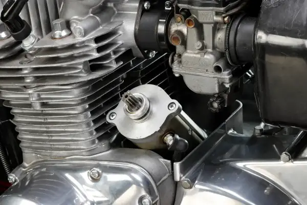 Dettaglio del motore di una moto: il test del motorino di avviamento è in primo piano, con il carburatore e le alette di raffreddamento visibili.