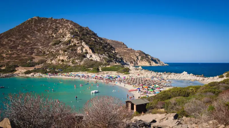 Una giornata di sole a Punta Molentis beach, con acque cristalline, sabbia dorata e tante persone che si godono il mare.