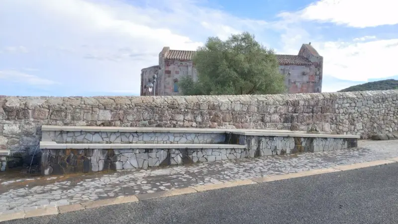 Fontana in pietra con scorci di un antico edificio religioso, un'oasi di pace ad **Allai, Sardegna**.