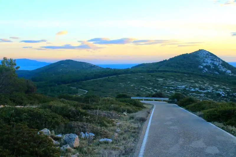 Strada panoramica verso il monte Doglia al tramonto, con colline verdi e cielo colorato.