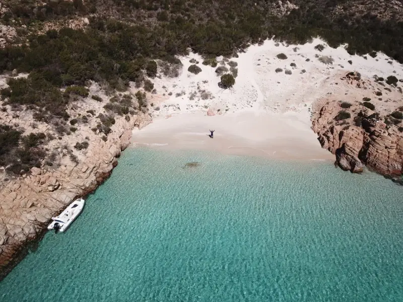 Una persona celebra la bellezza di Cala Soraya, con acque cristalline e rocce rosse. Una barca è ormeggiata.